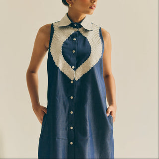Woman wearing a blue dress with a white embroidered collar against a neutral background