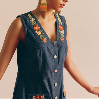 Woman wearing a denim dress with floral embroidery on a beige background